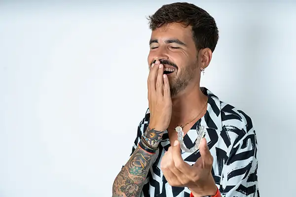 Tattooed man laughing while holding Invisalign, showcasing its ease of use for adults seeking straighter teeth.