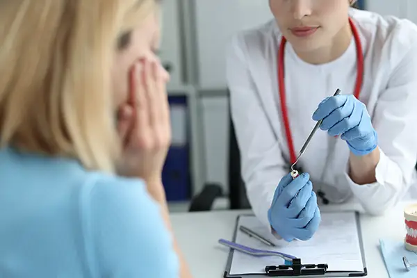 Dentist using a dental tool on a tooth model to explain a tooth issue to a concerned patient during an emergency consultation.